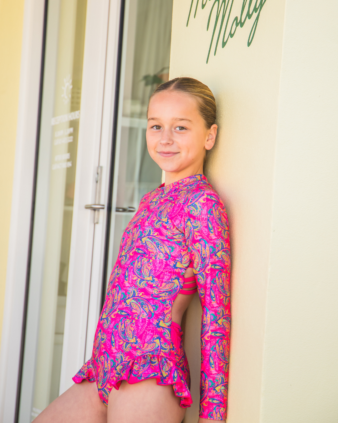 Young girl wearing a pink teen swimwear standing in front of a door.