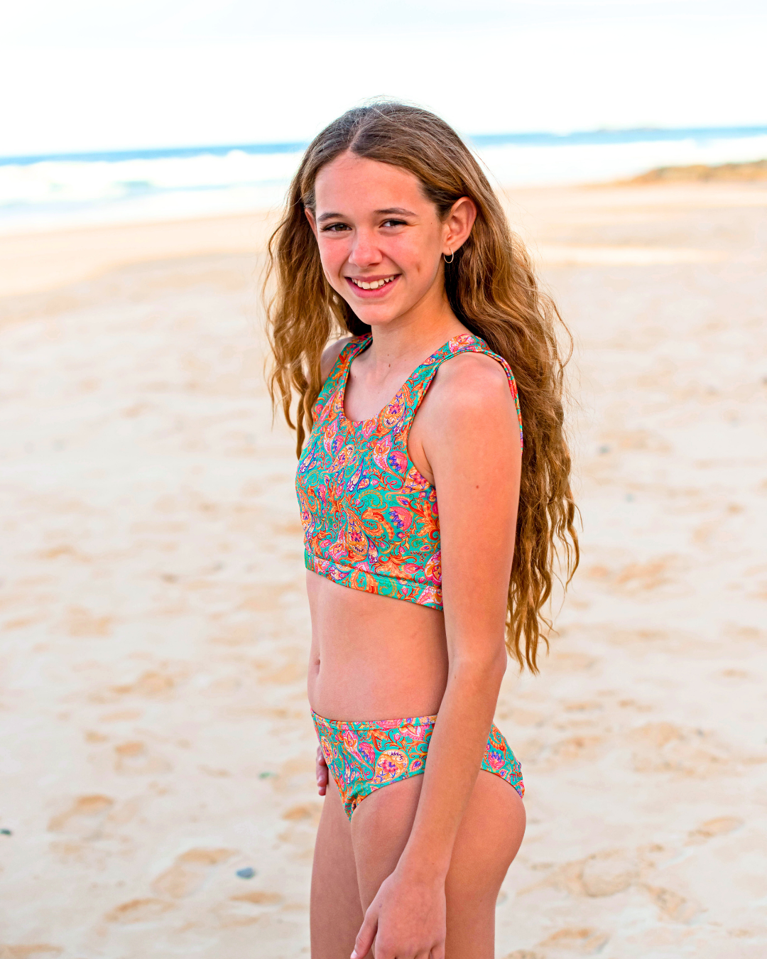 Young girl in a colorful teen bikini standing on a sandy beach.
