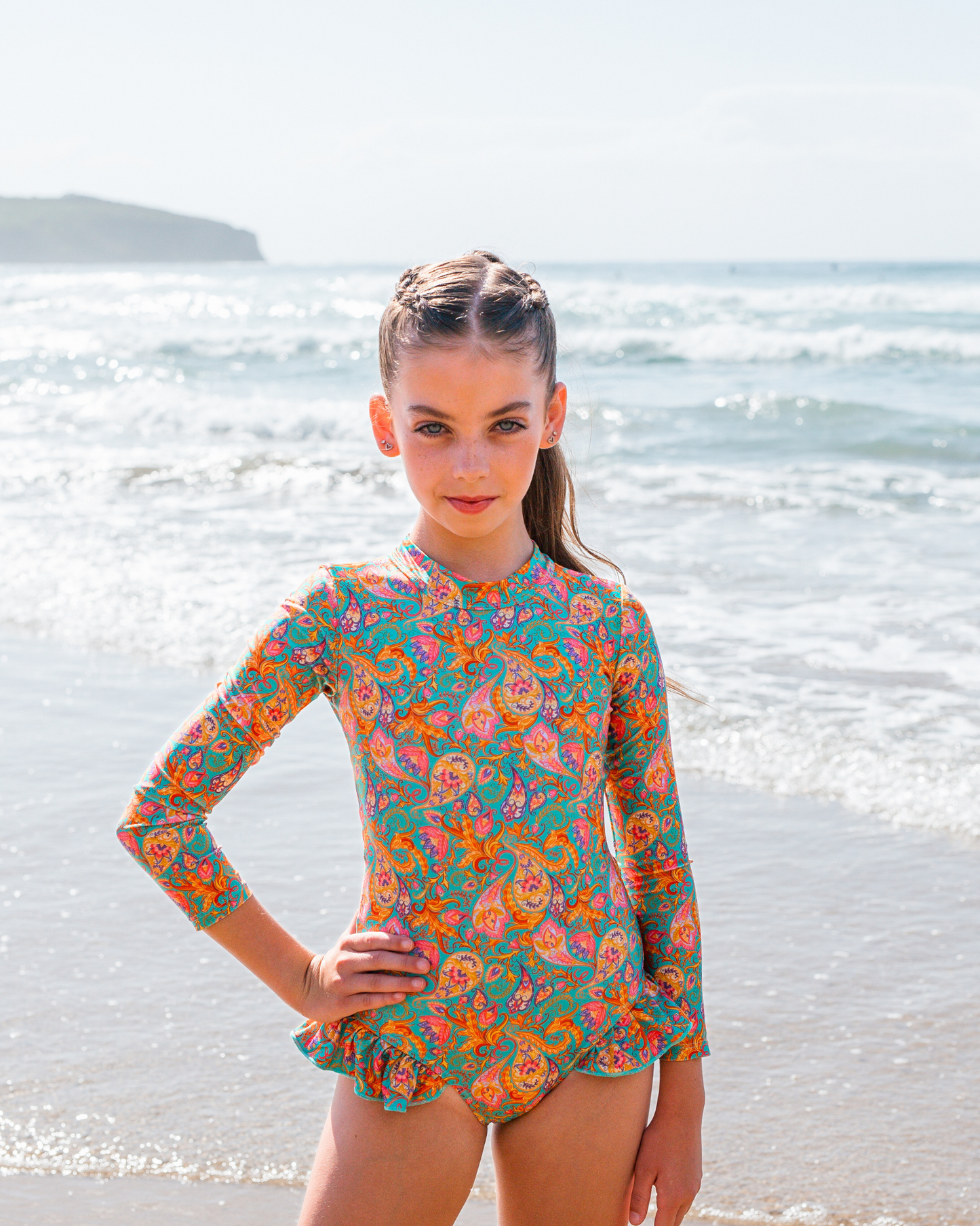 Young girl in a colorful girls swimwear standing on a beach with ocean in the background