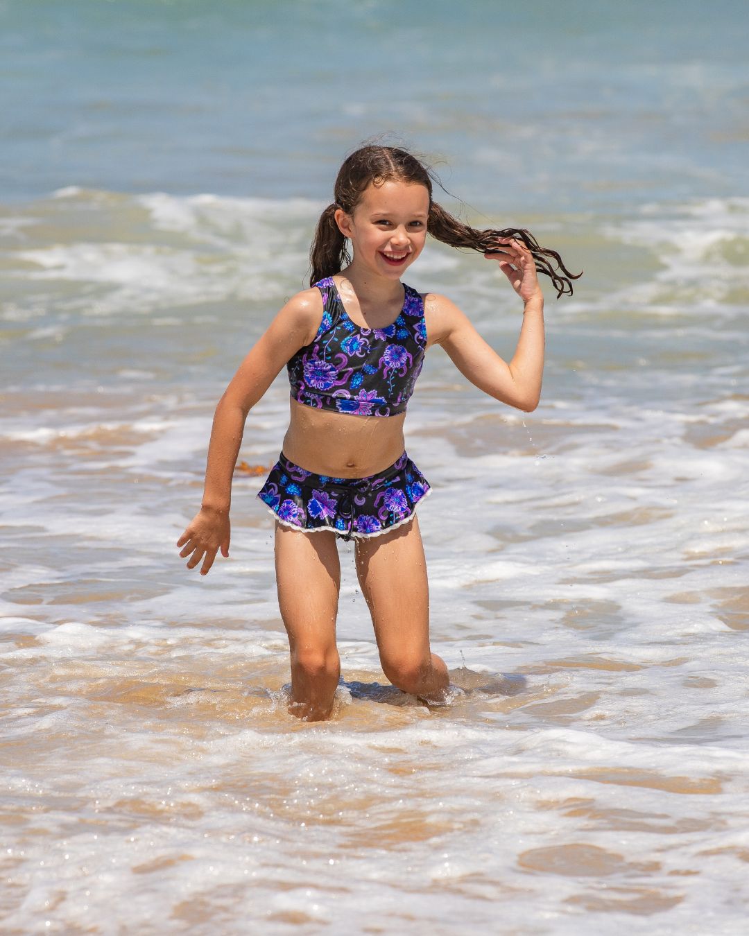 Young girl in a floral girls bathers standing in shallow water at the beach.