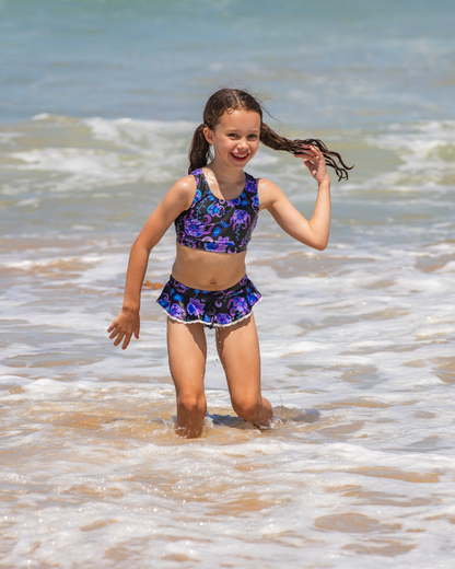 Young girl in a floral girls bathers standing in shallow water at the beach.