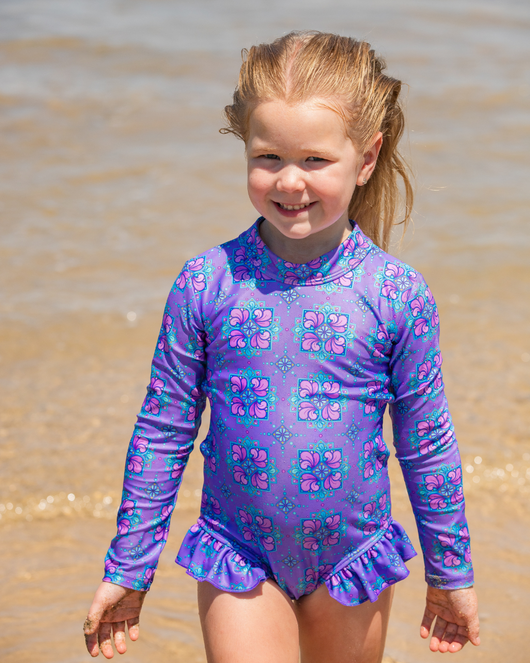 Young girl in a purple floral girls bathers standing on a beach.