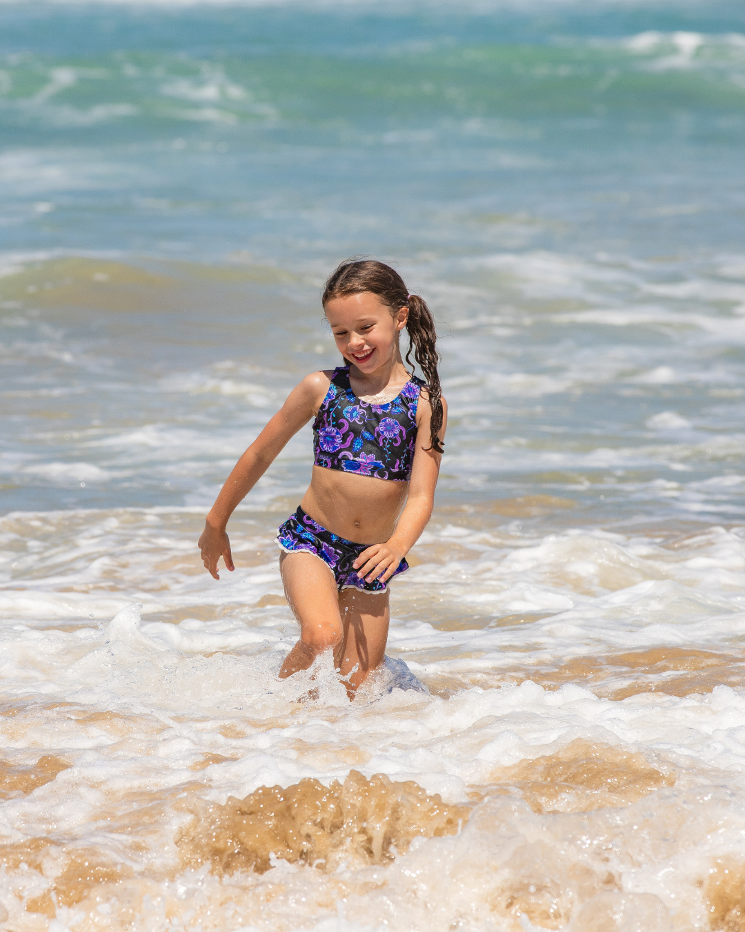 Young girl in a colorful girls swimsuit playing in the ocean waves.