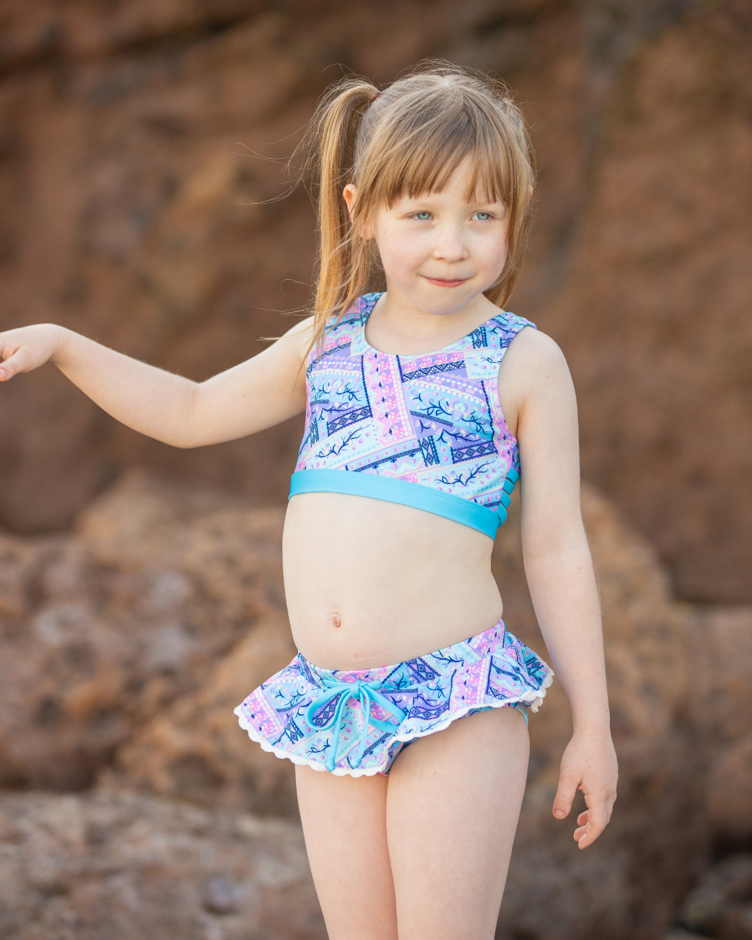Young girl wearing a colorful girls swimsuit standing against a rocky background