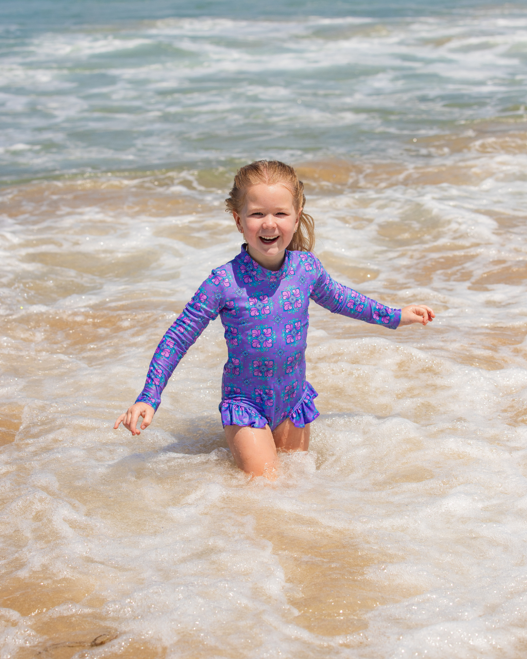 Young girl in a purple girls swimsuit playing in ocean waves