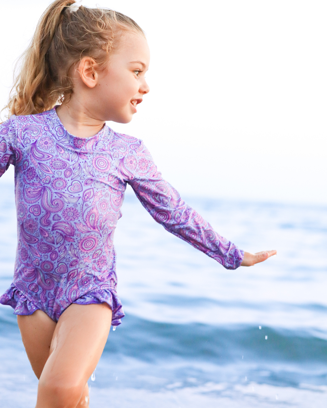 Young girl in girls swimsuit jumping through the waves