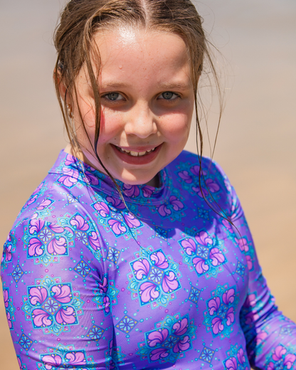 Young girl wearing a purple floral rgirls swimwear against a beige background