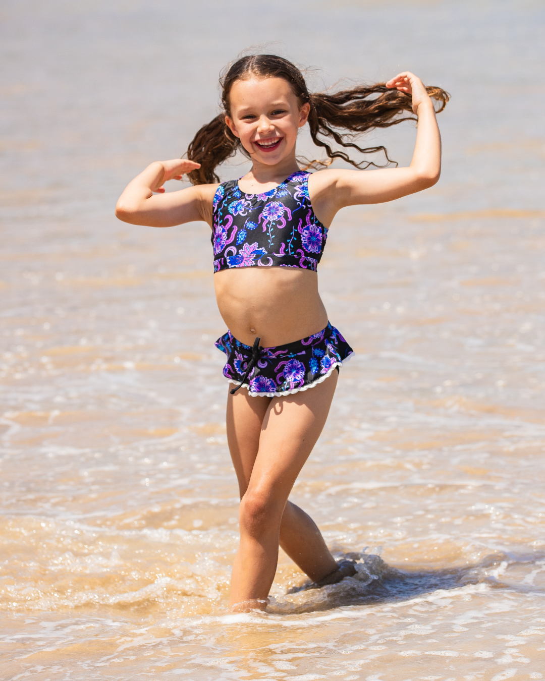 Young girl in a colorful girls bathers standing in shallow water at the beach.