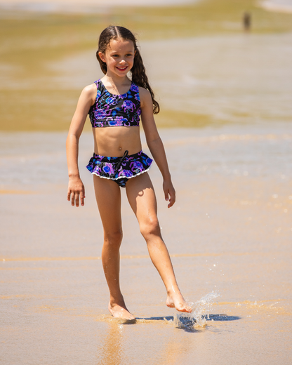 Young girl in a colorful girls bathers  standing in shallow water at a beach.