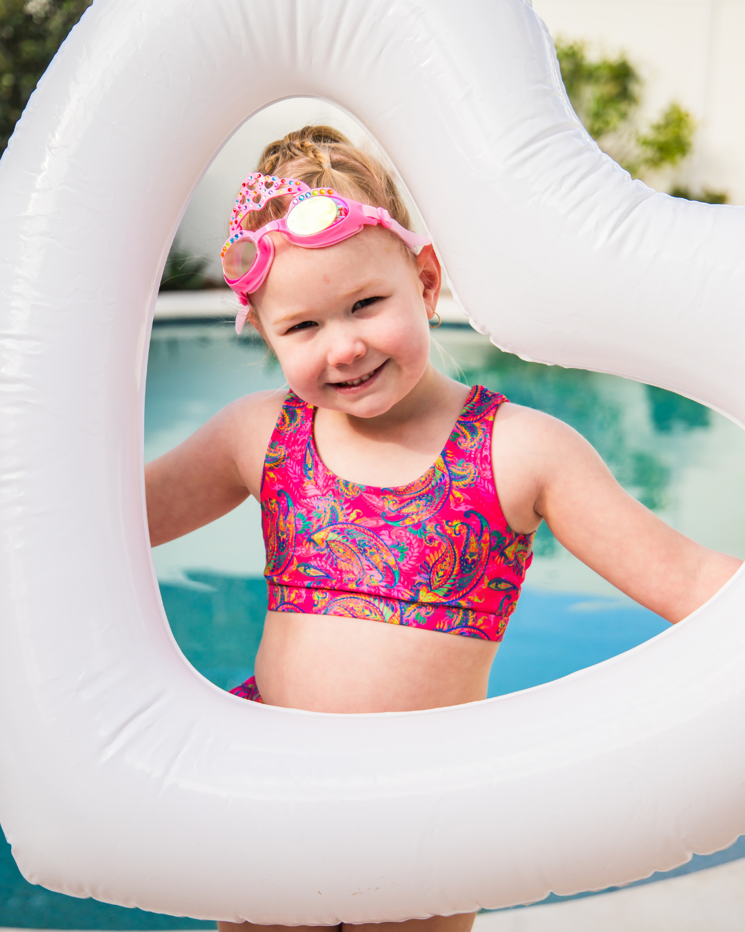Child in a colorful  girls swimsuit with a pink swim ring in a pool