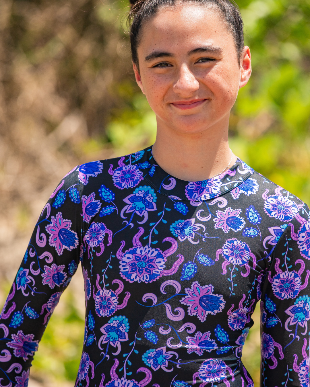 Person wearing a black girls one piece swimsuit with colorful floral patterns outdoors.