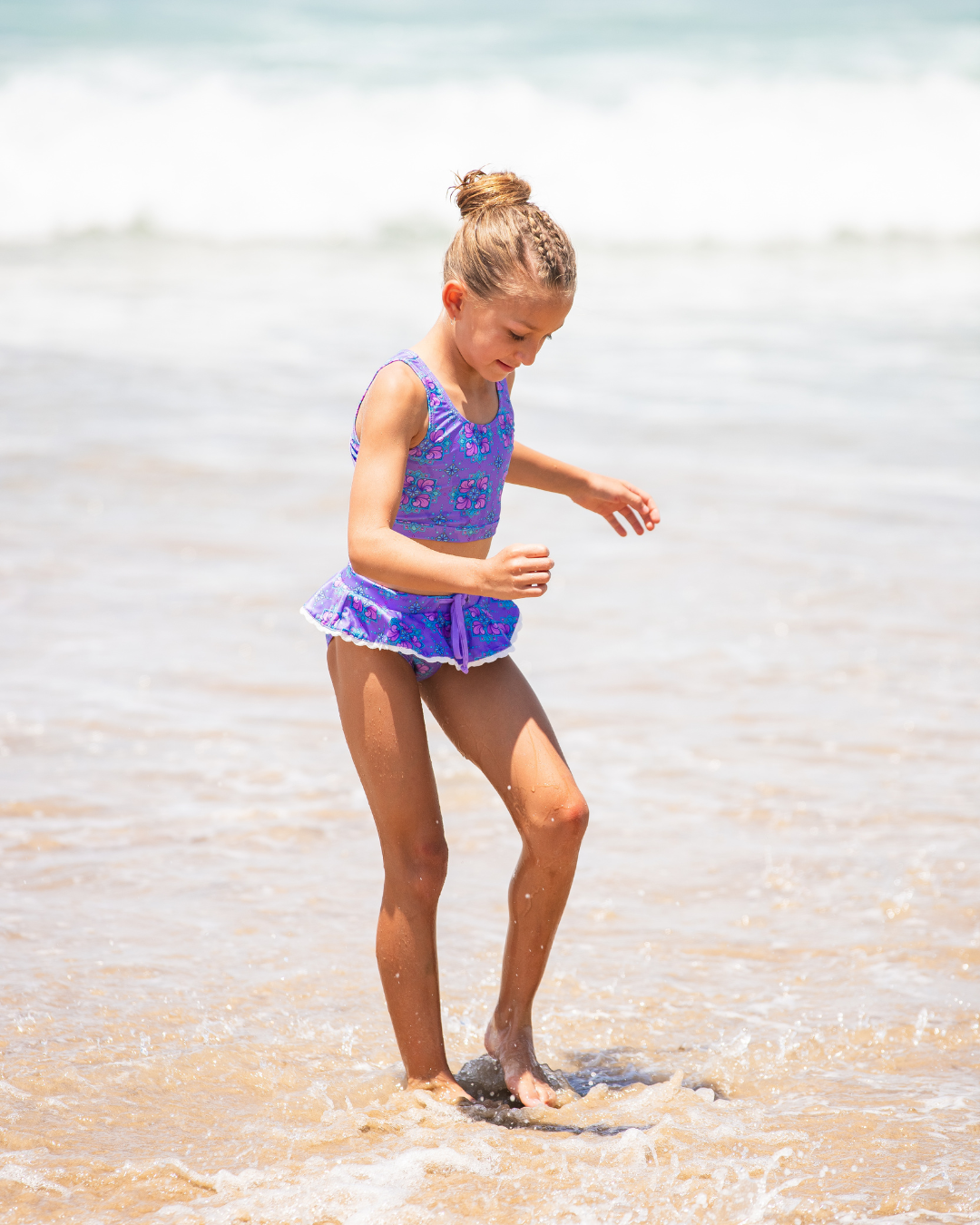 Young girl in a purple tween bikini playing in shallow water at the beach.