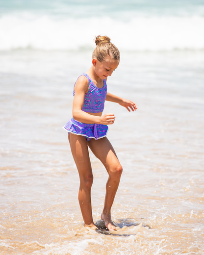 Young girl in a purple tween bikini playing in shallow water at the beach.