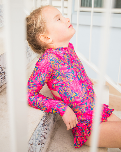 Child wearing a bright pink and multicolor patterned teen swimwear outfit sitting on a staircase.
