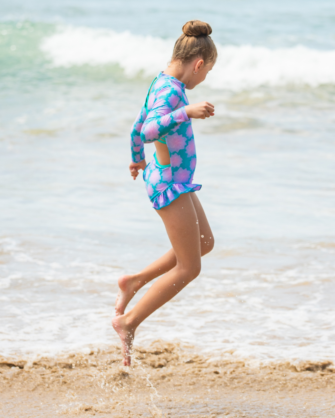 Child in a colorful girls bathers running on a beach with ocean waves in the background
