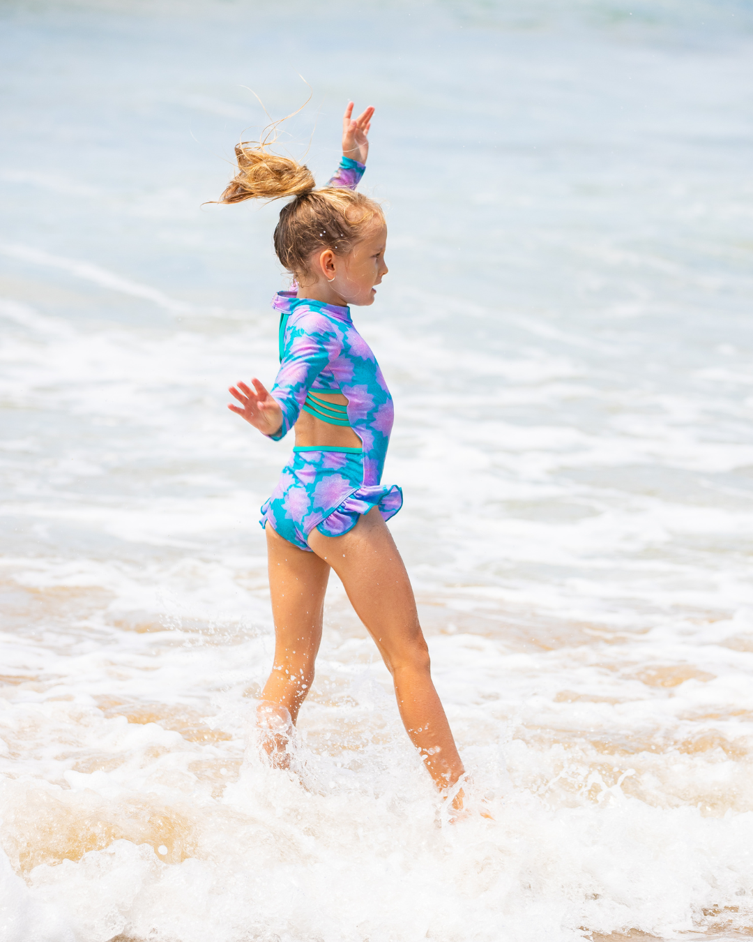 Child in a colorful girls one piece swimsuit playing in the ocean.