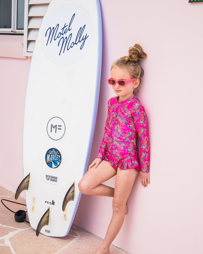 Child in a pink teen swimwear standing next to a Motel Molly surfboard.