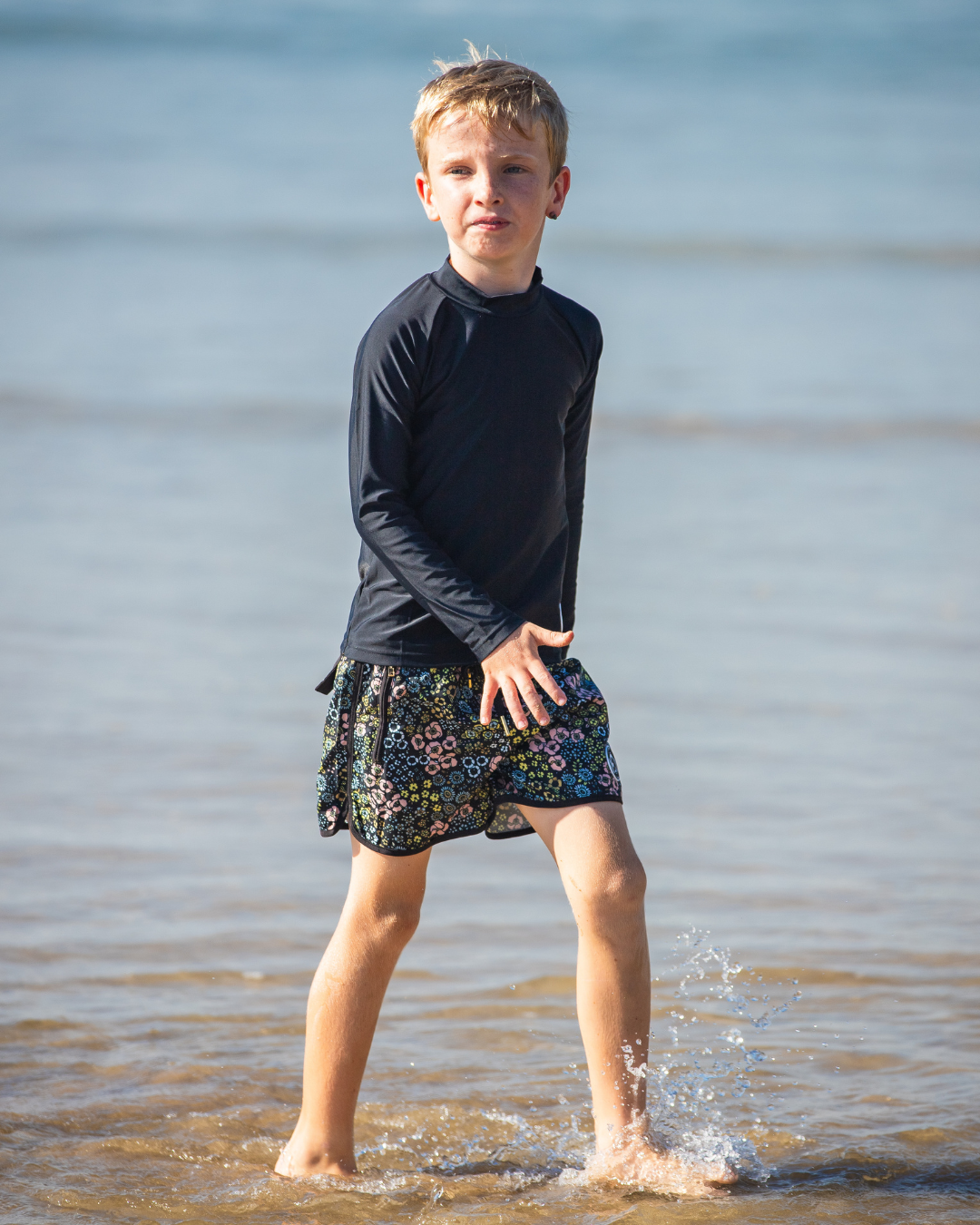 Child wearing a boys swimwear standing in shallow water at the beach.