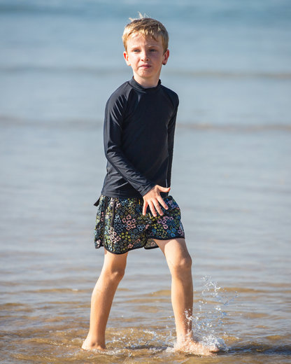 Child wearing a boys swimwear standing in shallow water at the beach.