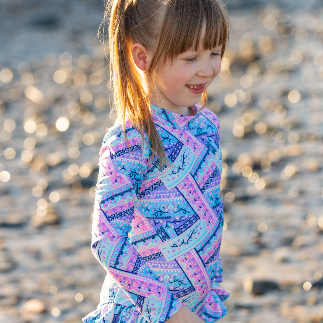 Young girl in a colorful patterned girls swimwear standing on a beach.