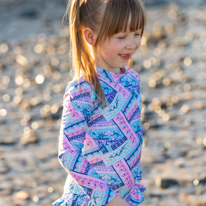 Young girl in a colorful patterned girls swimwear standing on a beach.
